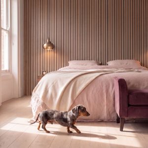 2.4m Chestnut Wall Panels installed behind a bed in a warm bedroom, with a dachshund walking across the floor.